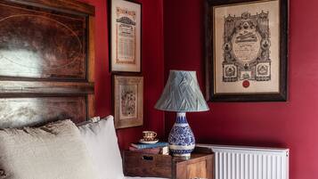 A bedroom with a wooden headboard, a white bed, a nightstand with a lamp, and framed certificates on the wall.