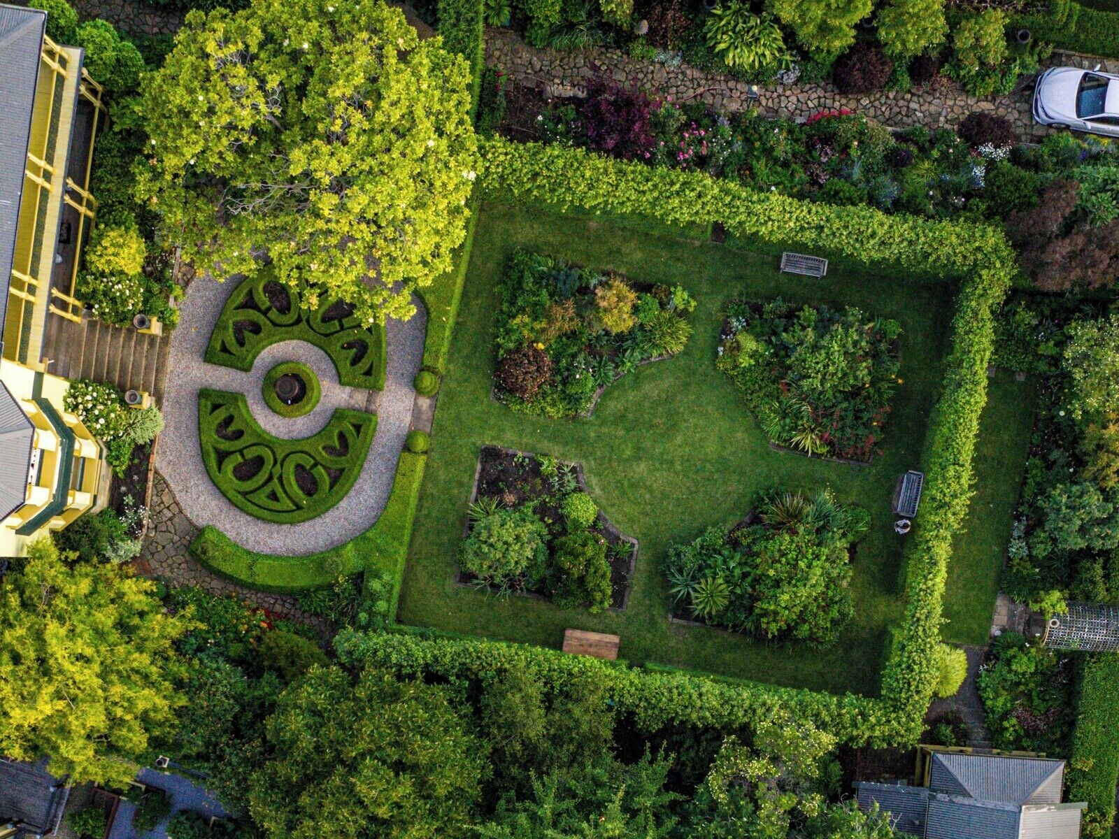 Vista aérea de un jardín bien cuidado con un seto circular central, rodeado de diversas plantas y árboles.