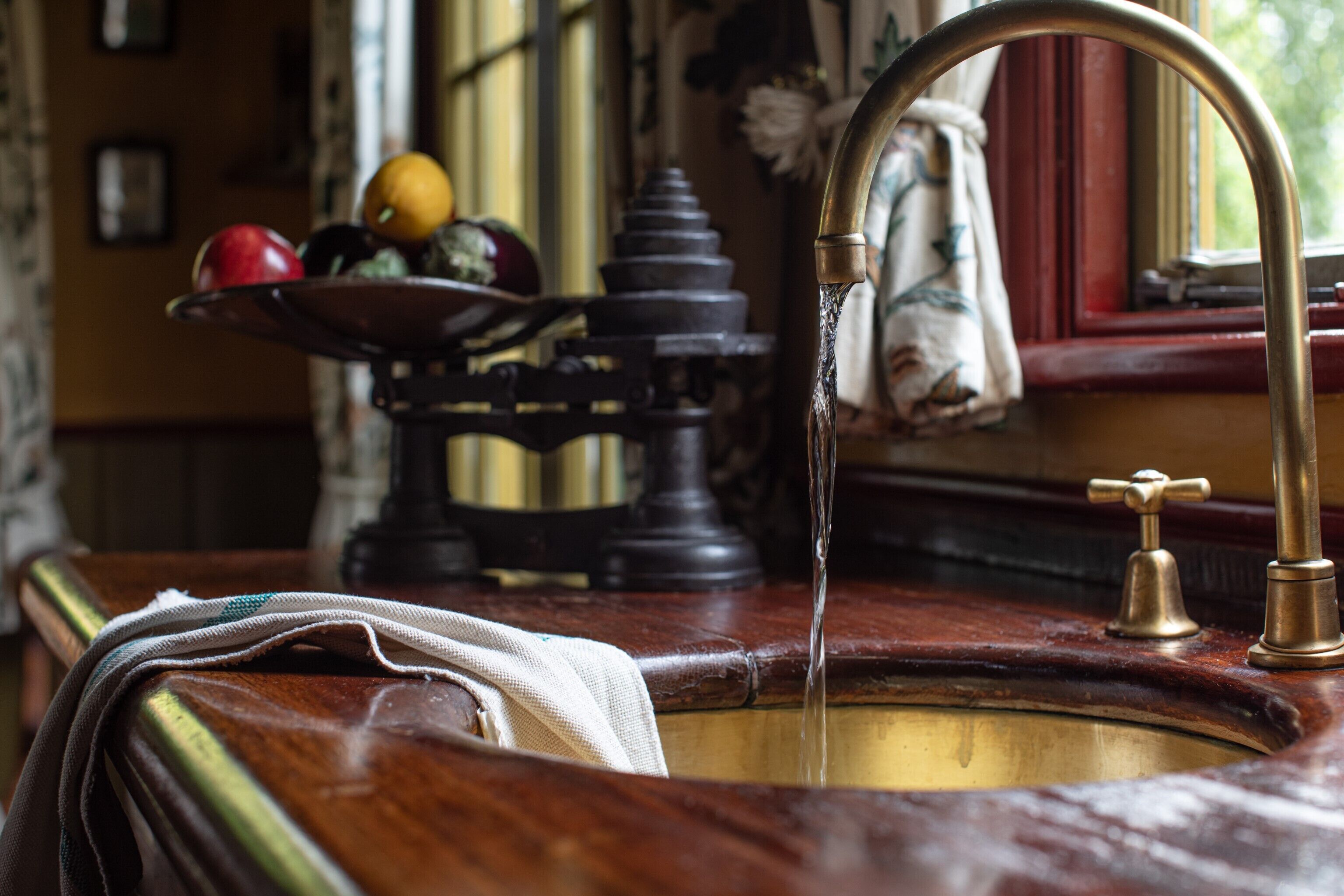 Un lavamanos antiguo de cocina con grifo de latón, encimera de madera y frutero con manzanas y naranjas.