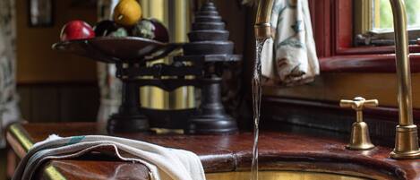 Un lavamanos antiguo de cocina con grifo de latón, encimera de madera y frutero con manzanas y naranjas.