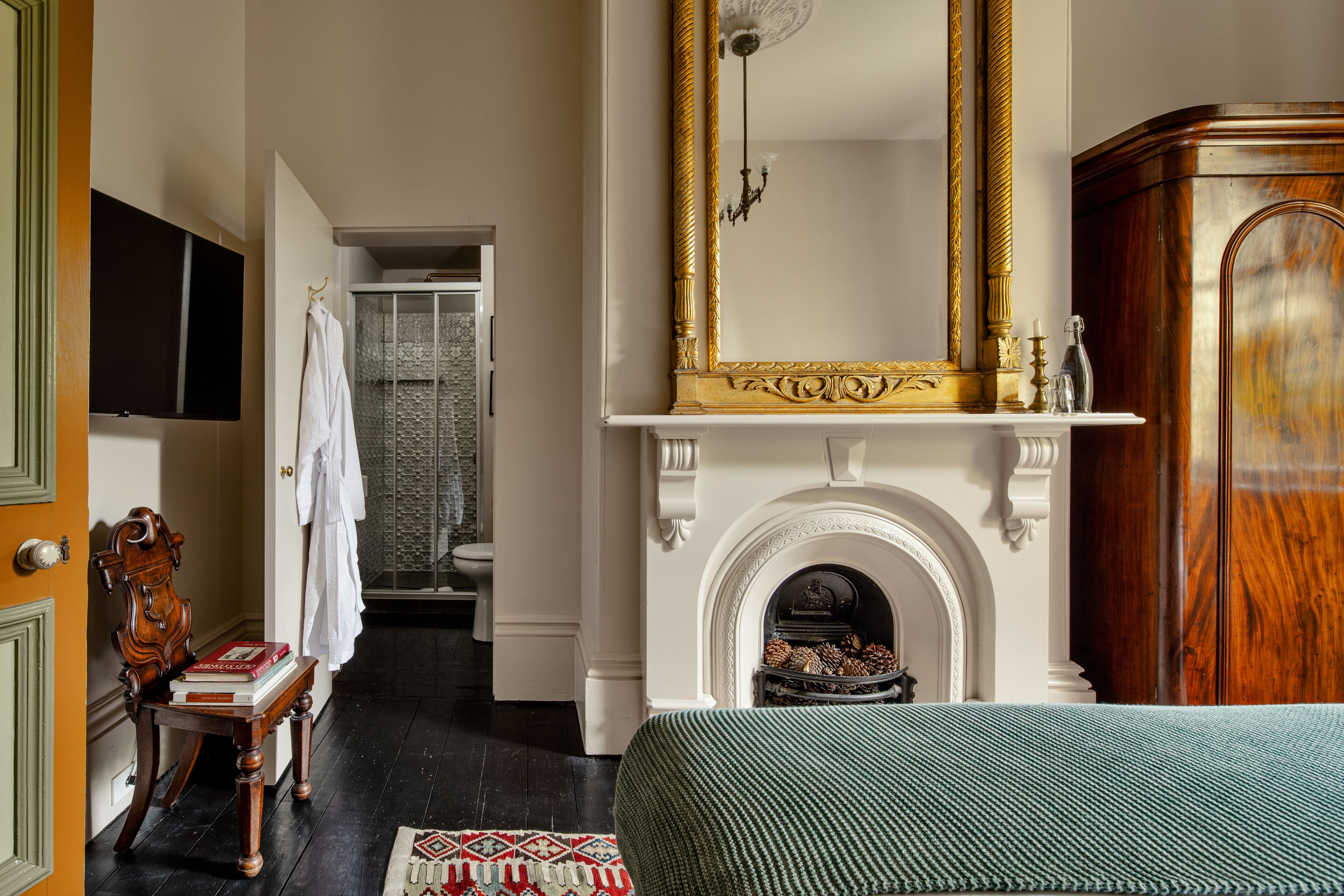 Een slaapkamer met een open haard, een grote spiegel en een houten garderobe.