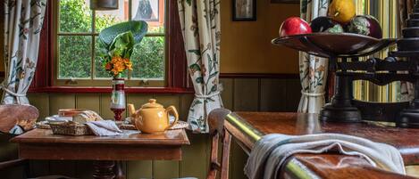 A cozy room with a wooden table, a window with curtains, and a fruit bowl on a stand.