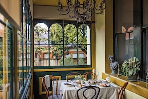 A dining area with a table set for four, a chandelier, and a view of a garden through a window.