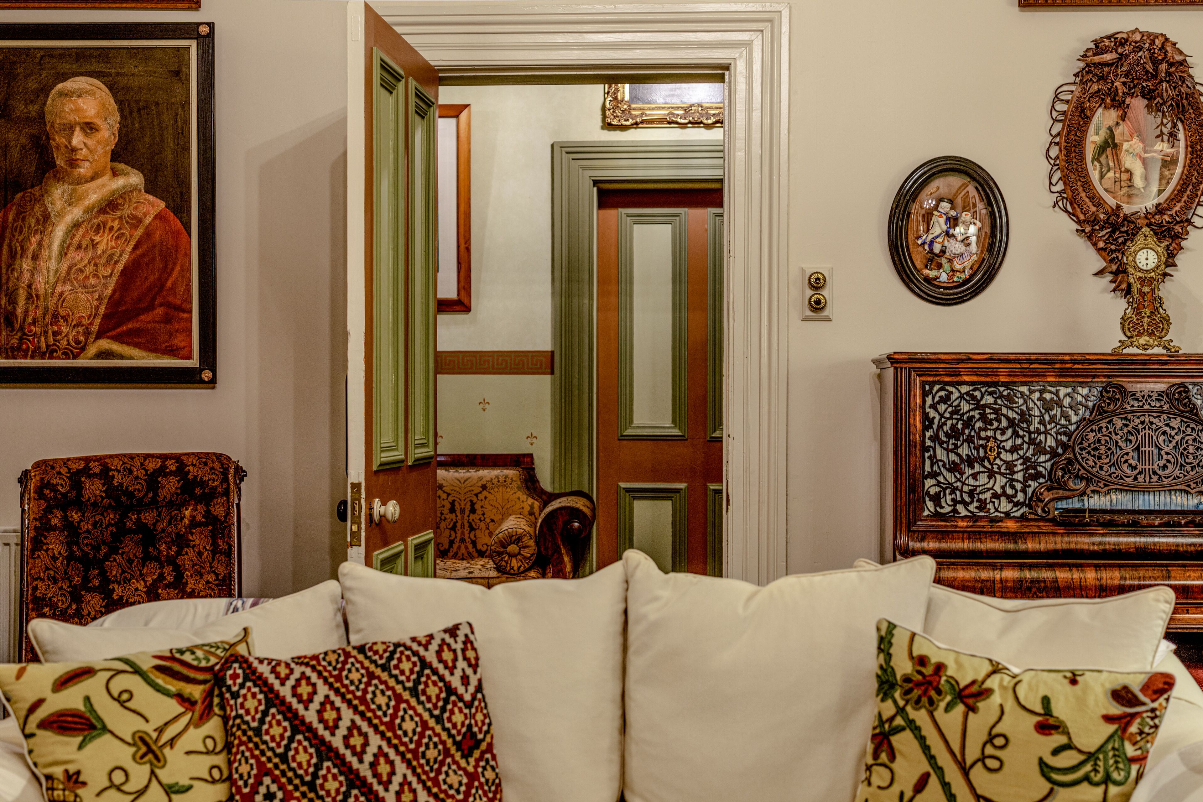 A living room with a sofa, patterned cushions, a framed portrait, a mirror, and a clock on a wooden cabinet.