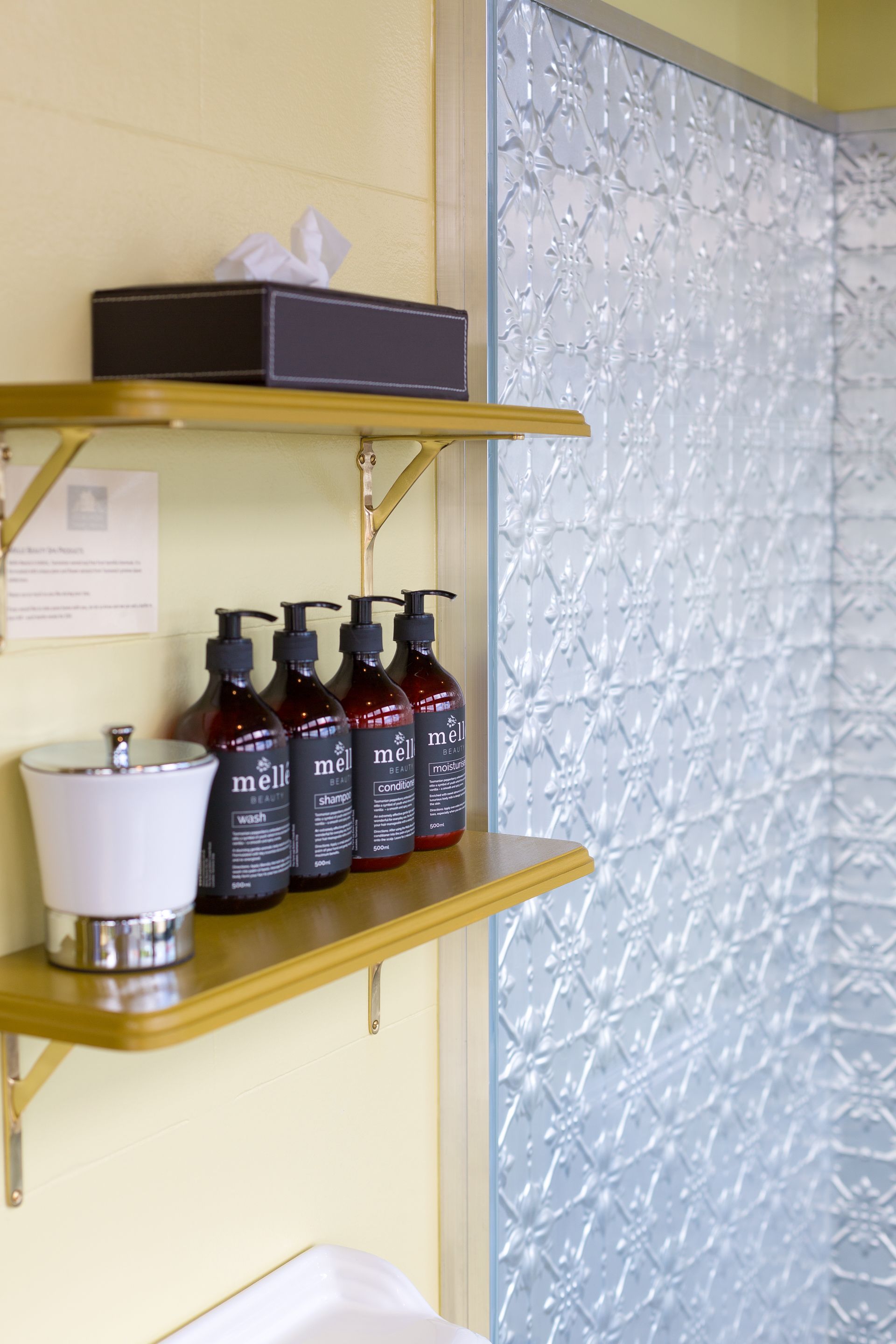 Et badeværelse med en hylde med Mielle shampoo og conditioner, en hvid vask og en tissueskasse.