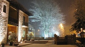 A snow-covered courtyard with a stone building, a tree, and a well-lit pathway. - Hotel & Spa María Manuela (Onis)