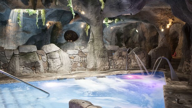 A hot tub with a rocky cave-like background, a stone wall, and a waterfall feature. - Hotel & Spa María Manuela (Onis)