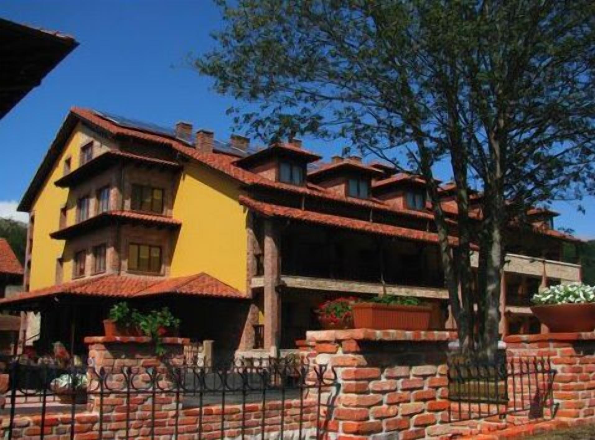 A multi-story building with a yellow facade and red-tiled roofs, surrounded by brick walls and potted plants.