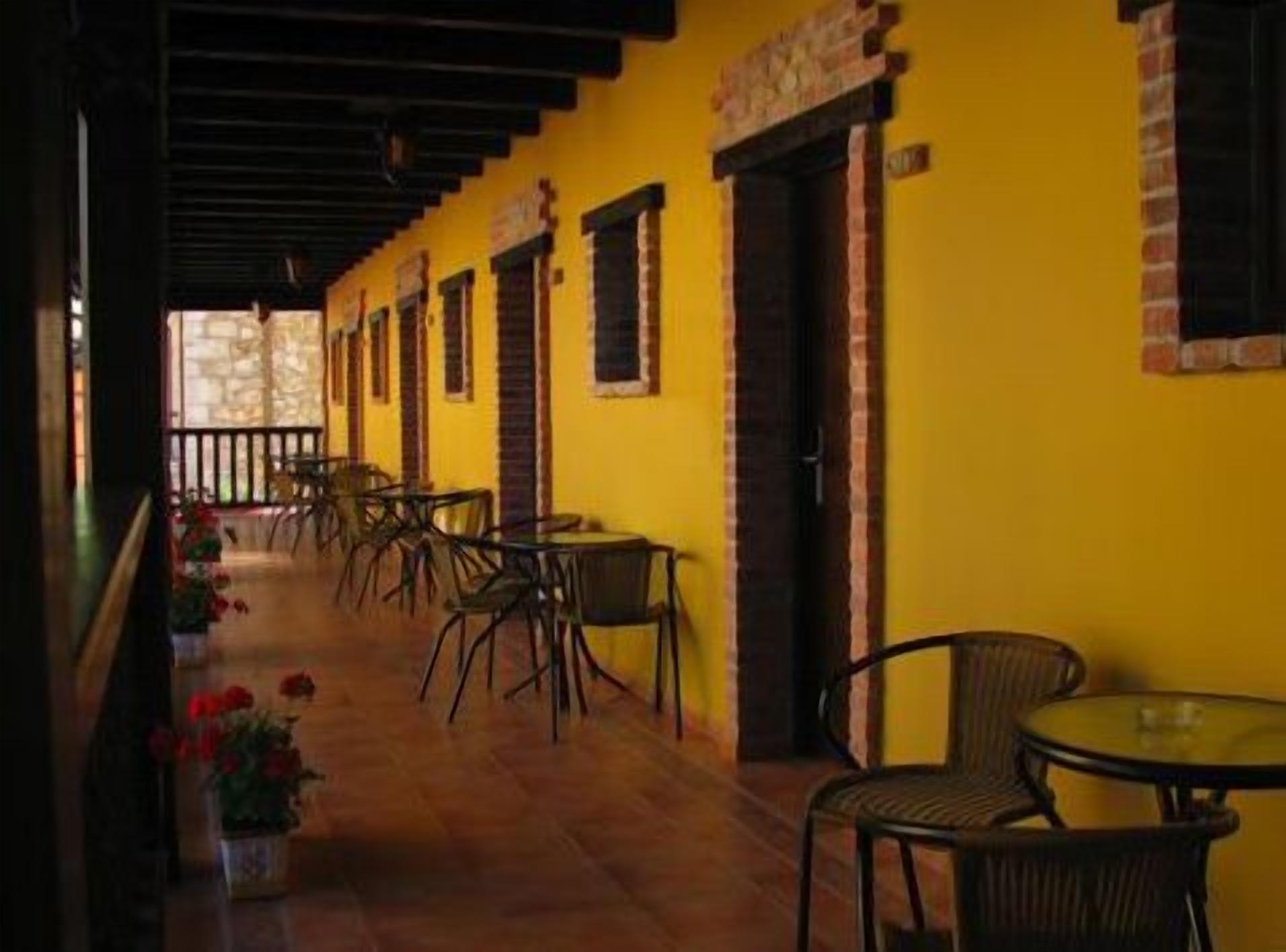 Un pasillo con paredes amarillas y detalles de ladrillo, bordeado por mesas y sillas, que sugiere un comedor o sala de estar.
