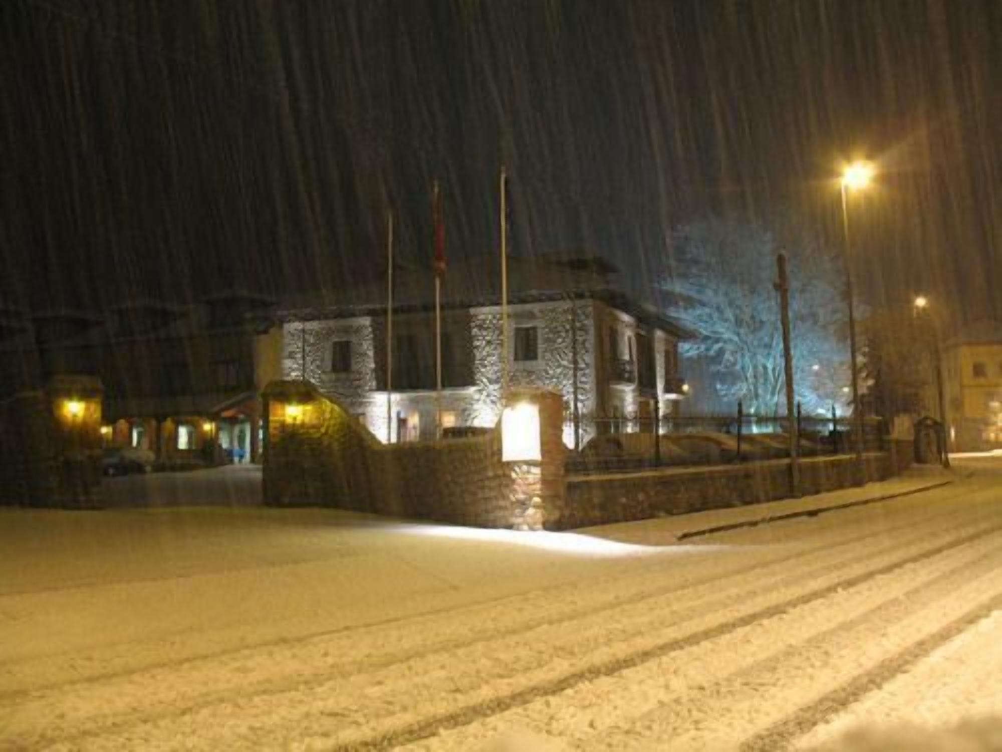 Une rue enneigée, de nuit, avec un bâtiment dont la façade est en pierre et l’entrée est illuminée.