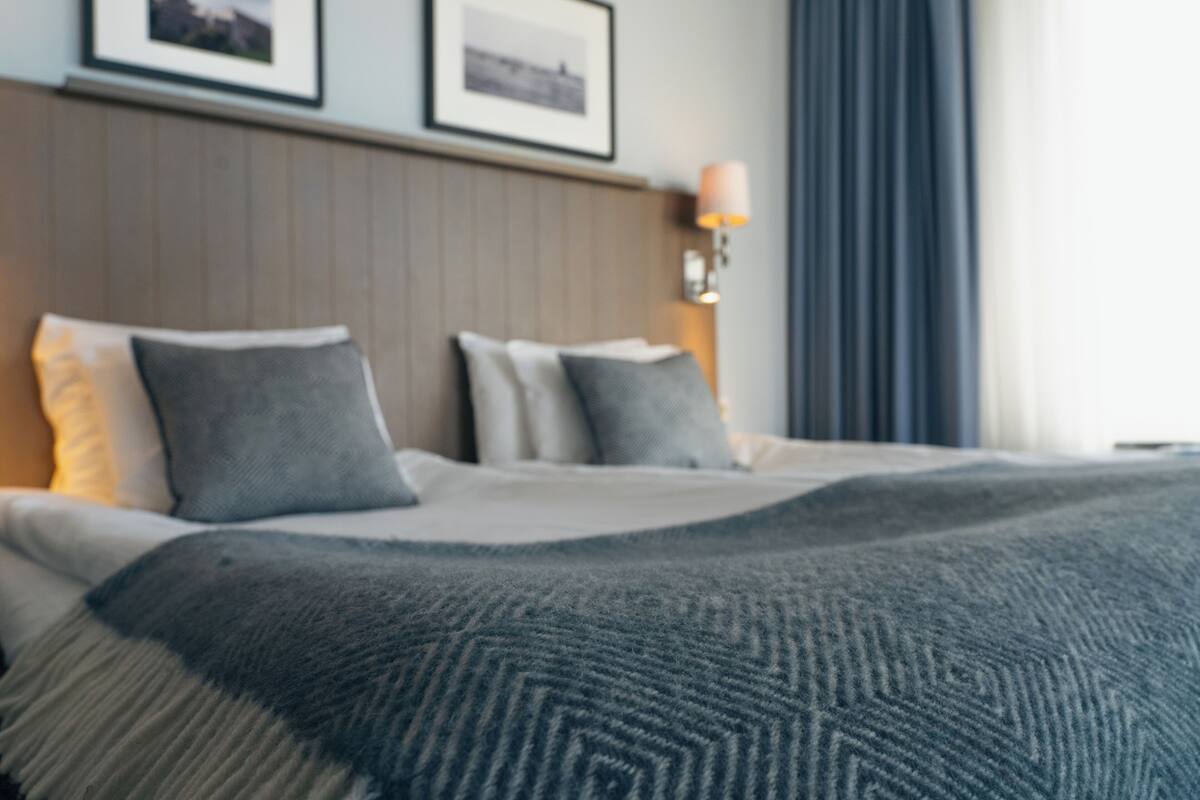 A hotel room with a bed, pillows, a lamp, and framed pictures on the wall.