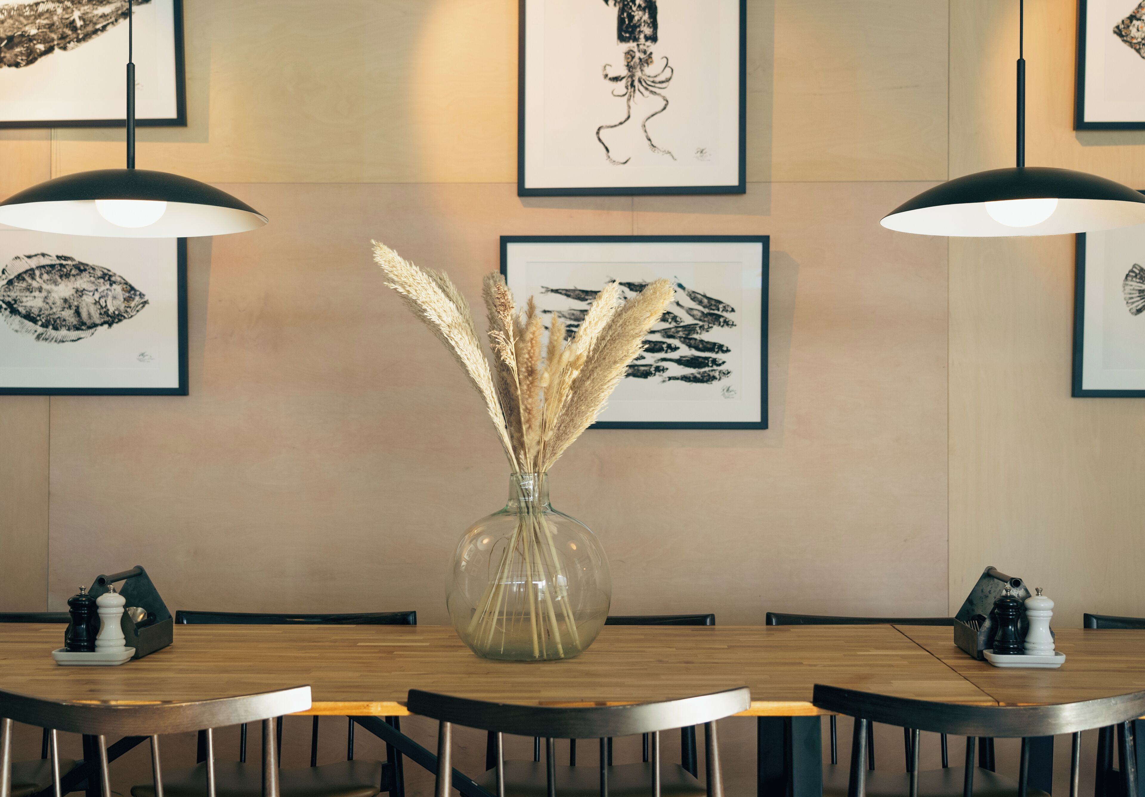 A dining area with a round wooden table, black chairs, and a vase with dried plants.