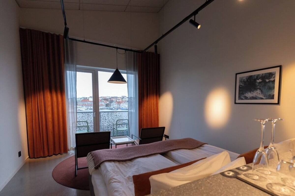 A hotel room with a bed, a desk, a chair, a window with curtains, and a framed picture on the wall.