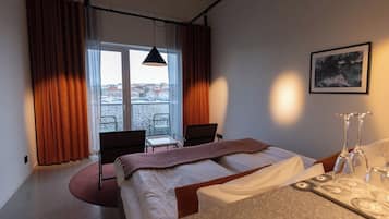 Ett hotellrum med en säng, ett skrivbord, en stol, ett fönster med gardiner och en inramad tavla på väggen.