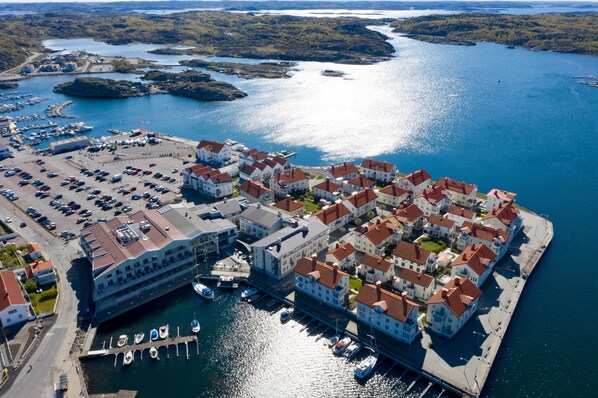 An aerial view of a coastal town with a marina, waterfront buildings, and a road leading to the harbor.