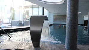 An indoor swimming pool with a modern design, featuring a large water feature and a glass wall providing a view of the outside. - Marstrands Havshotell (Marstrand)