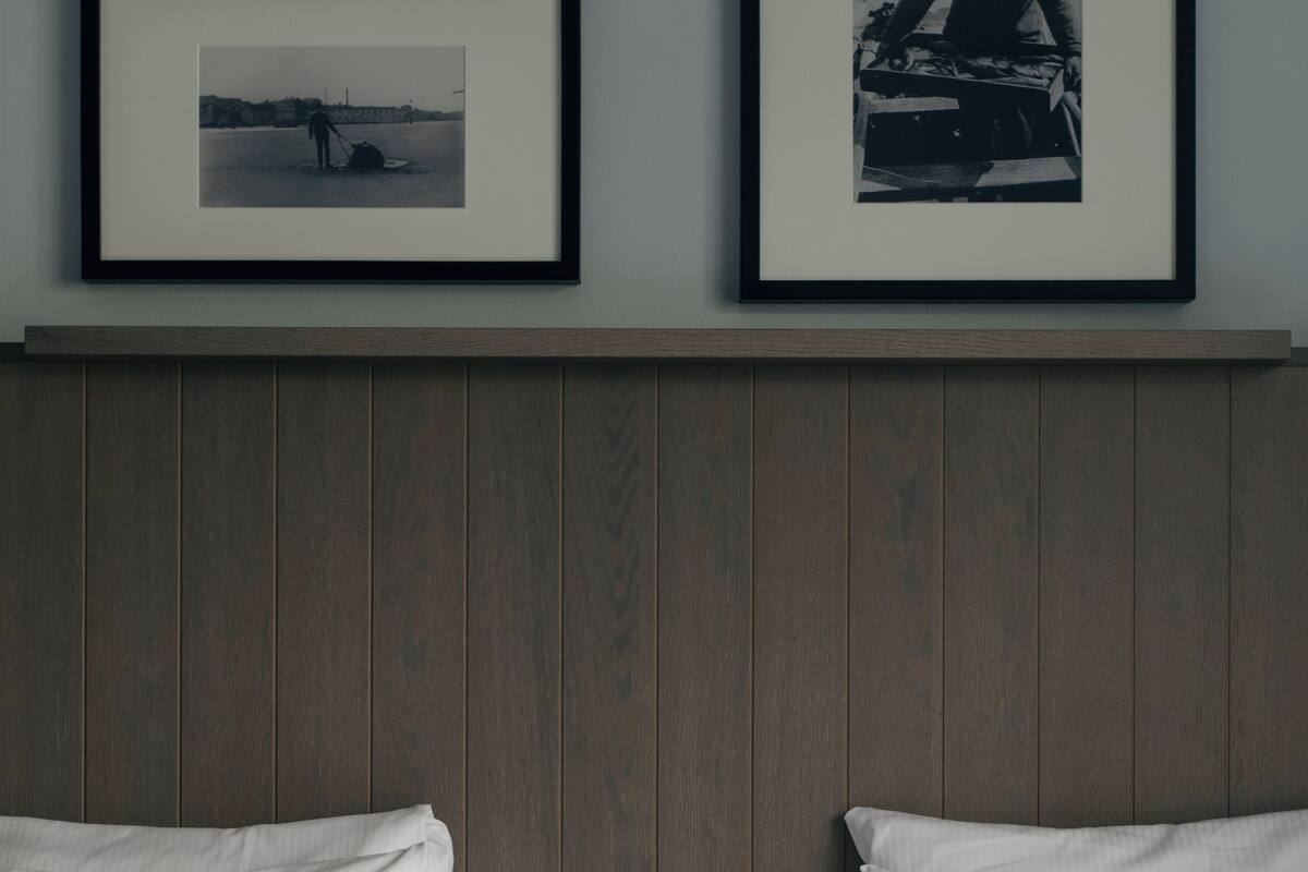 A hotel room with a wooden headboard, two white beds, and two framed pictures on the wall.