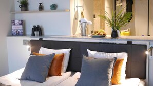A neatly arranged bedroom with a bed, pillows, a bedside table with a lamp, and a shelf with decorative items. - Marstrands Havshotell (Marstrand)