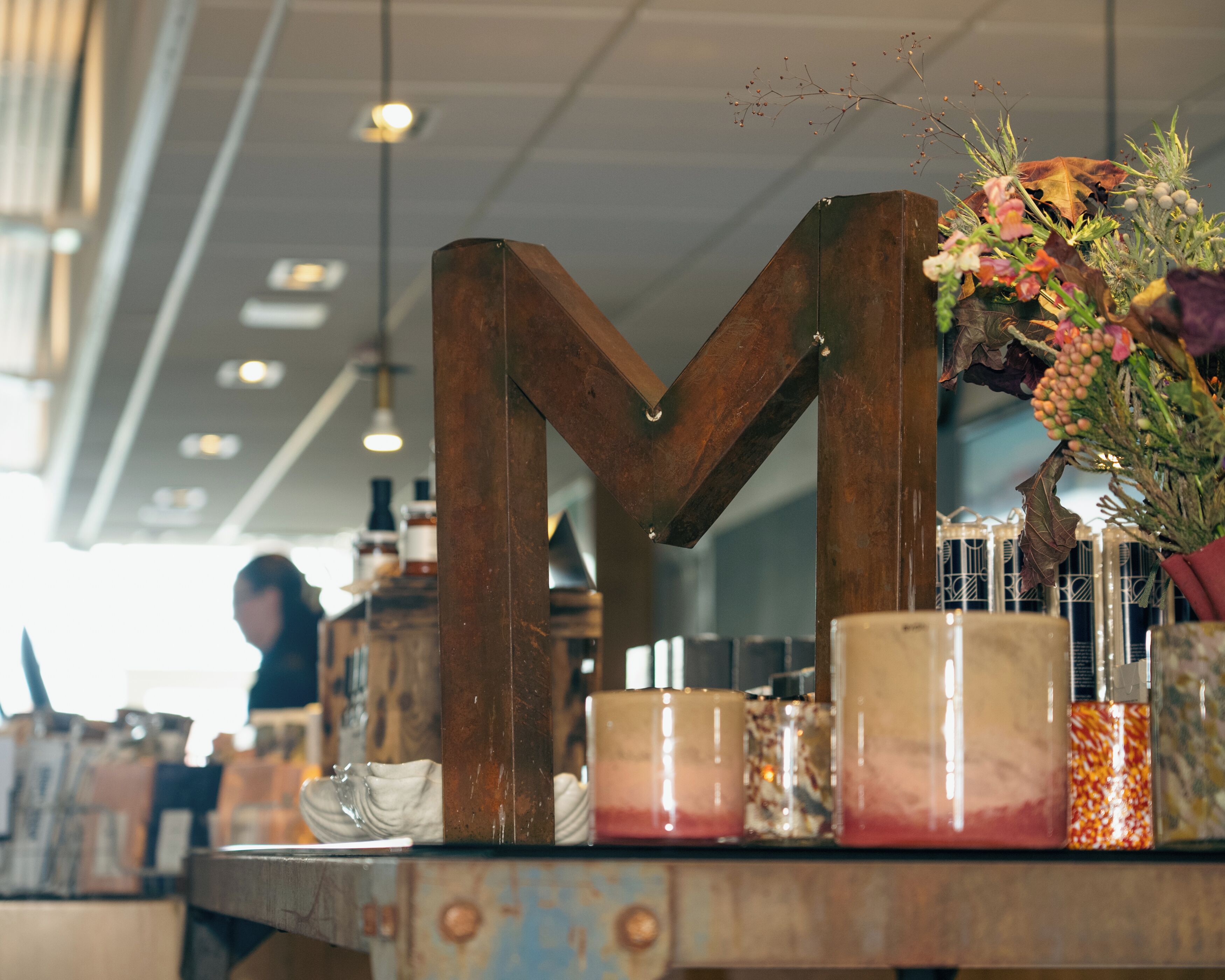 Una letra 'M' de madera como centro de mesa en una tabla con varios objetos, incluyendo un florero y velas.