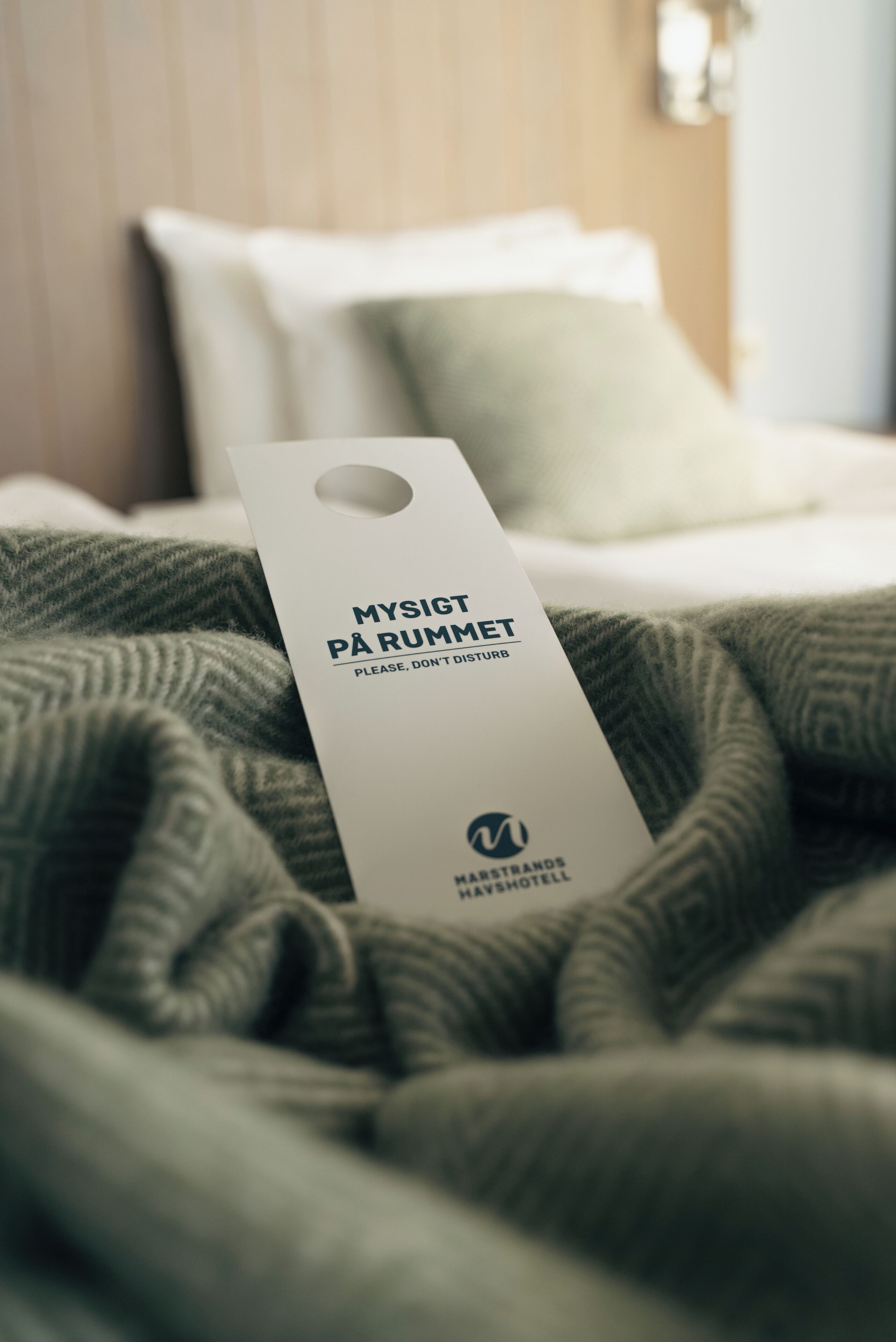 Une étiquette sur un lit portant l’inscription « MYSIGT PÅ RUMMET, NE PAS DÉRANGER » et le logo de l’hôtel Harstrands Havshotell.