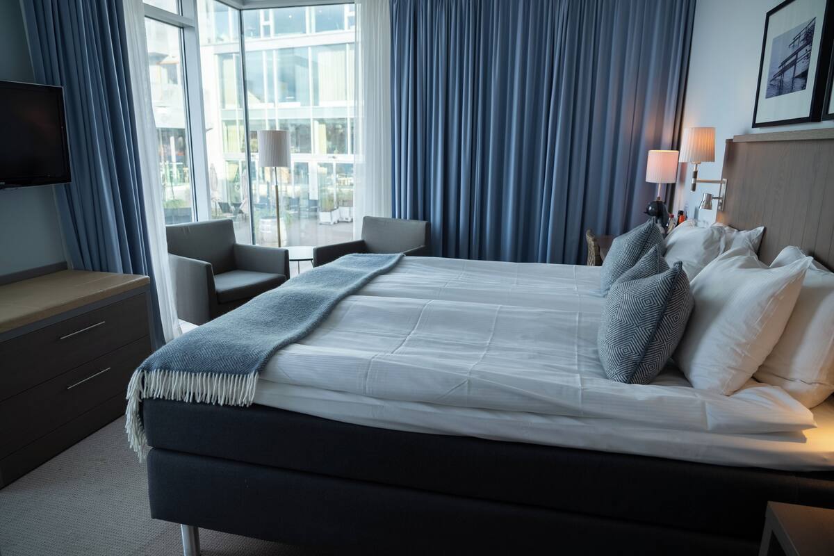 A hotel room with a bed, a desk, a chair, a TV, and a window with curtains.