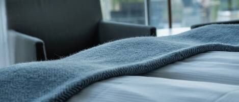 A modern hotel room with a large window, a bed with a grey blanket, and a floor lamp.