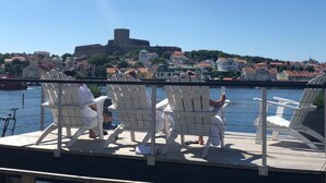 A deck with white chairs overlooking a body of water, a historic building in the background, and a clear sky. - Marstrands Havshotell (Marstrand)