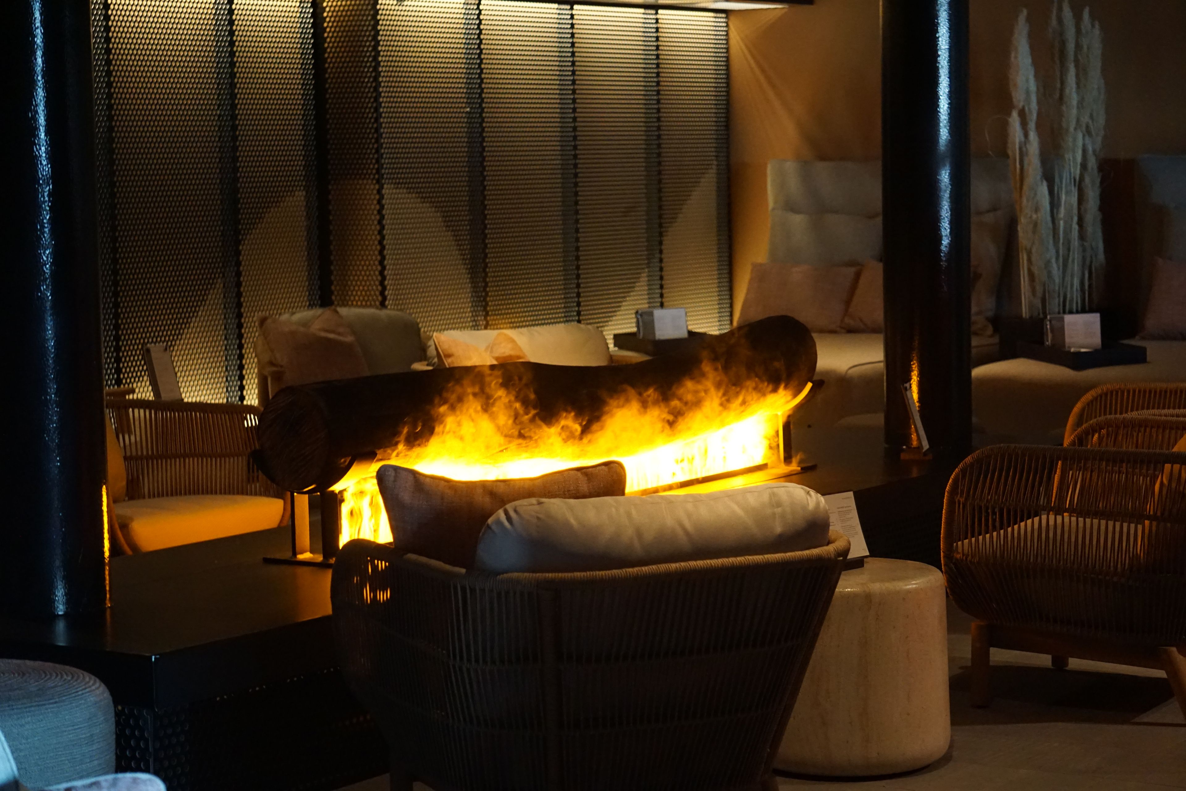 A room with a sofa, a coffee table, and a fireplace with a fire.