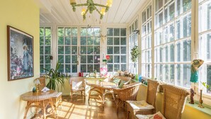 Ein sonnendurchflutetes Zimmer mit Korbmöbeln, großen Fenstern und einem Bild an der Wand.