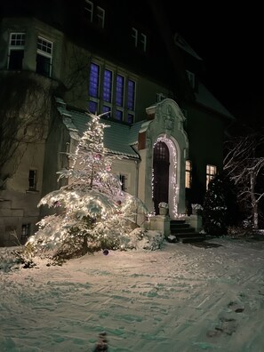 Een besneeerd landschap met een verlichte kerstboom en een gebouw met een opvallende bogenpoort.