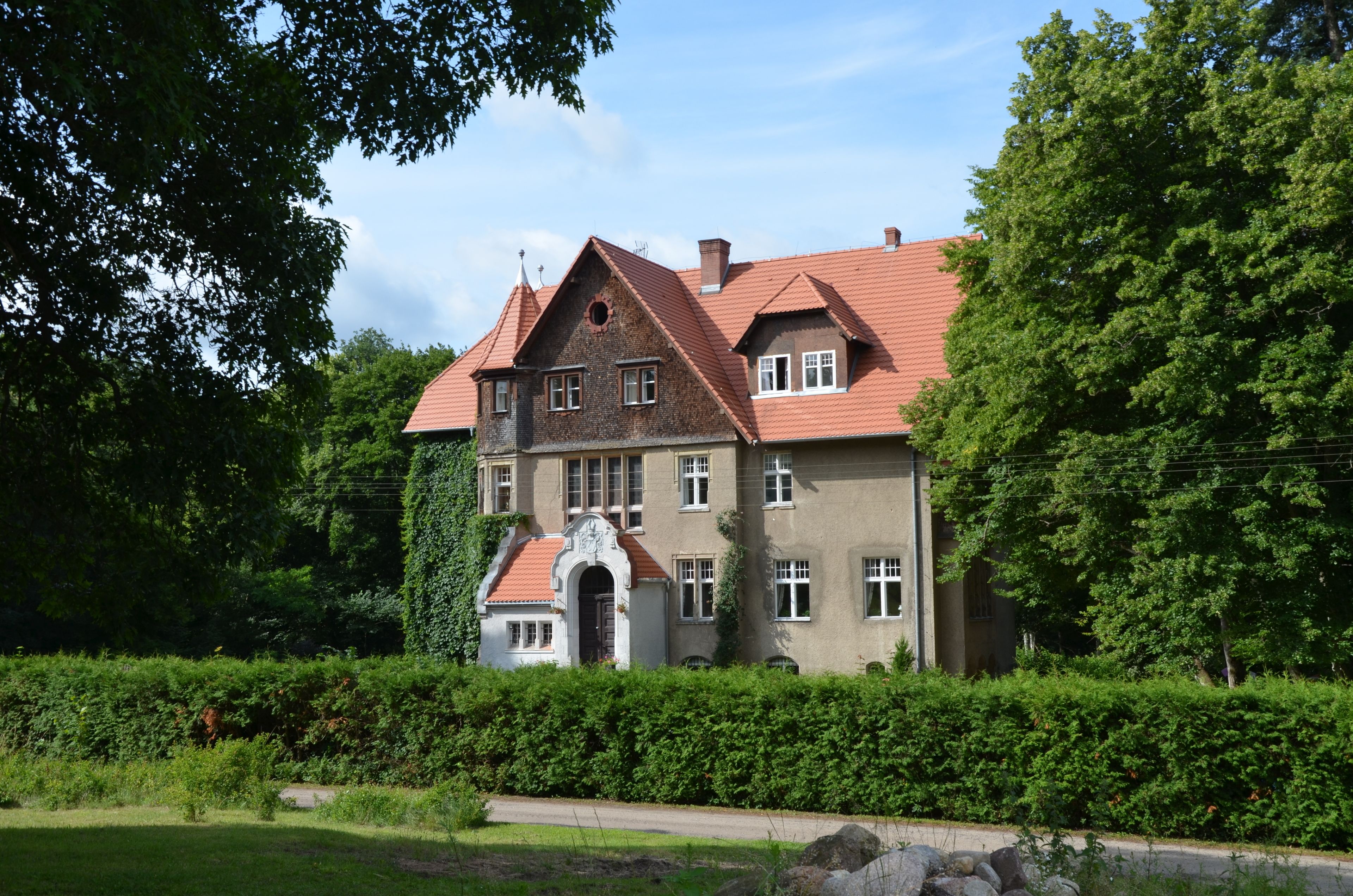 A large, historic building with a red-tiled roof, multiple windows, and a prominent entrance.