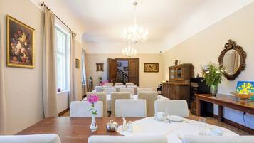 Ruokailutilassa on puinen pöytä, johon on katettu neljälle, ja pöydän ympärillä on valkoisia tuoleja. Kattolampetti roikkuu katosta, ja seinillä on kehystettyjä tauluja.
