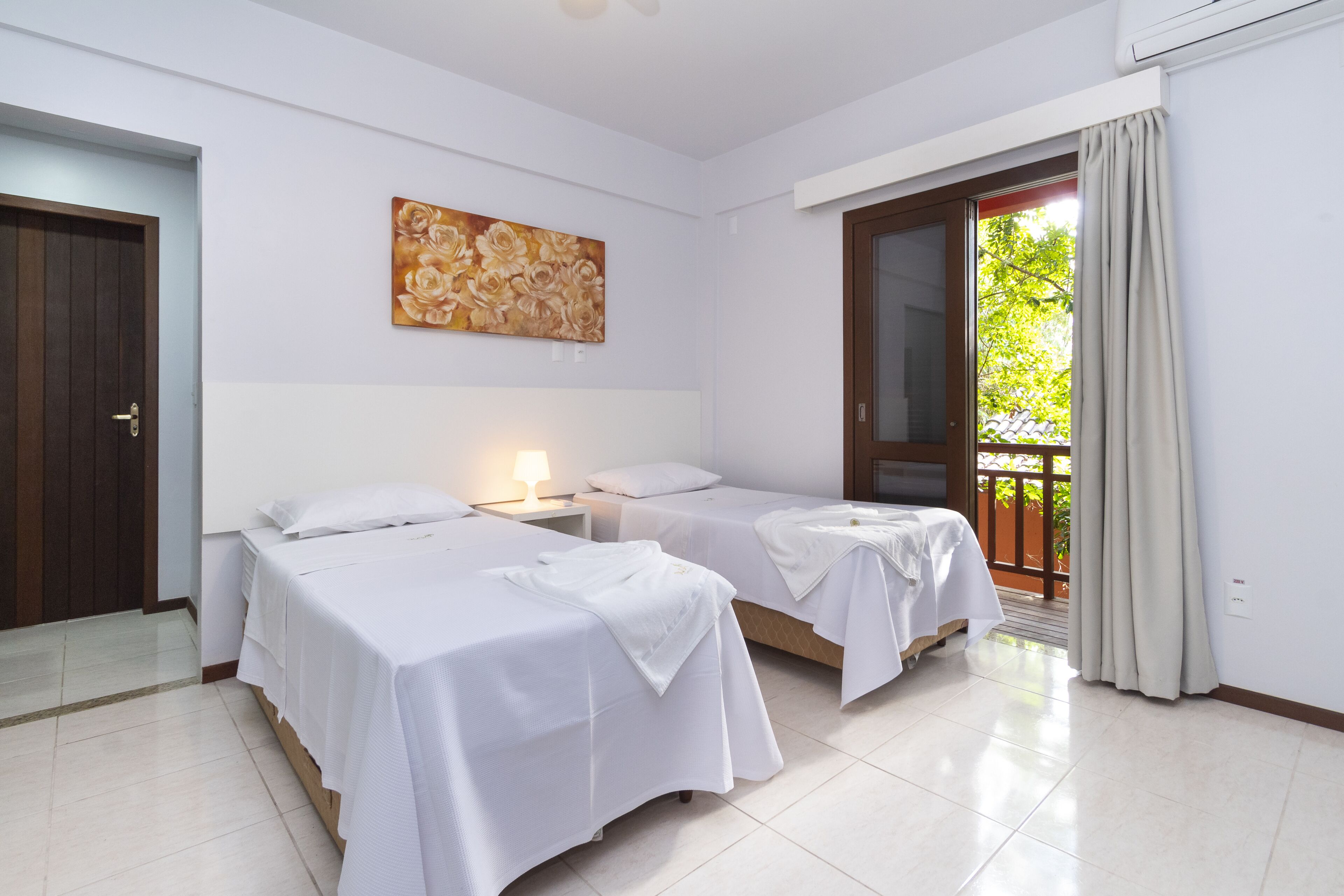 A hotel room with two beds, a painting on the wall, a nightstand, and a sliding glass door to the outside.