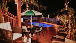 Un área de piscina al aire libre con terraza de madera, sillas de descanso y una mesa con botellas.