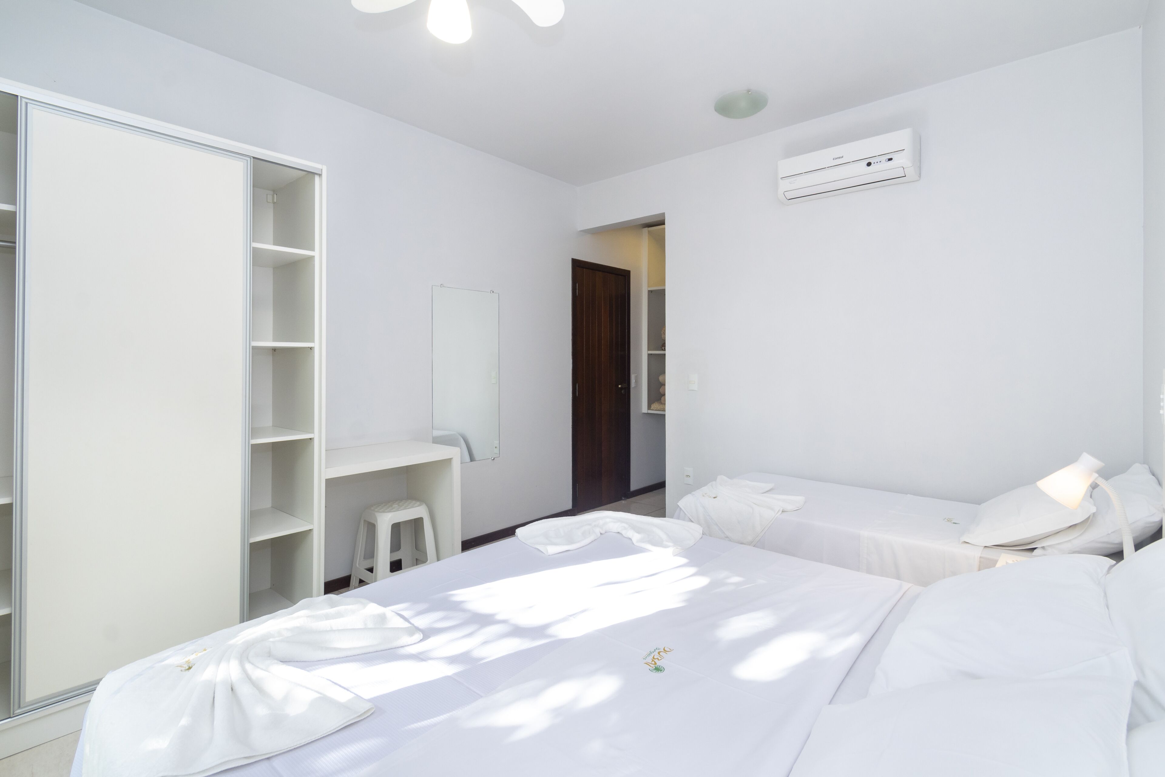 A modern hotel room with a large wardrobe, a desk, a bed with white linens, and an air conditioning unit on the wall.