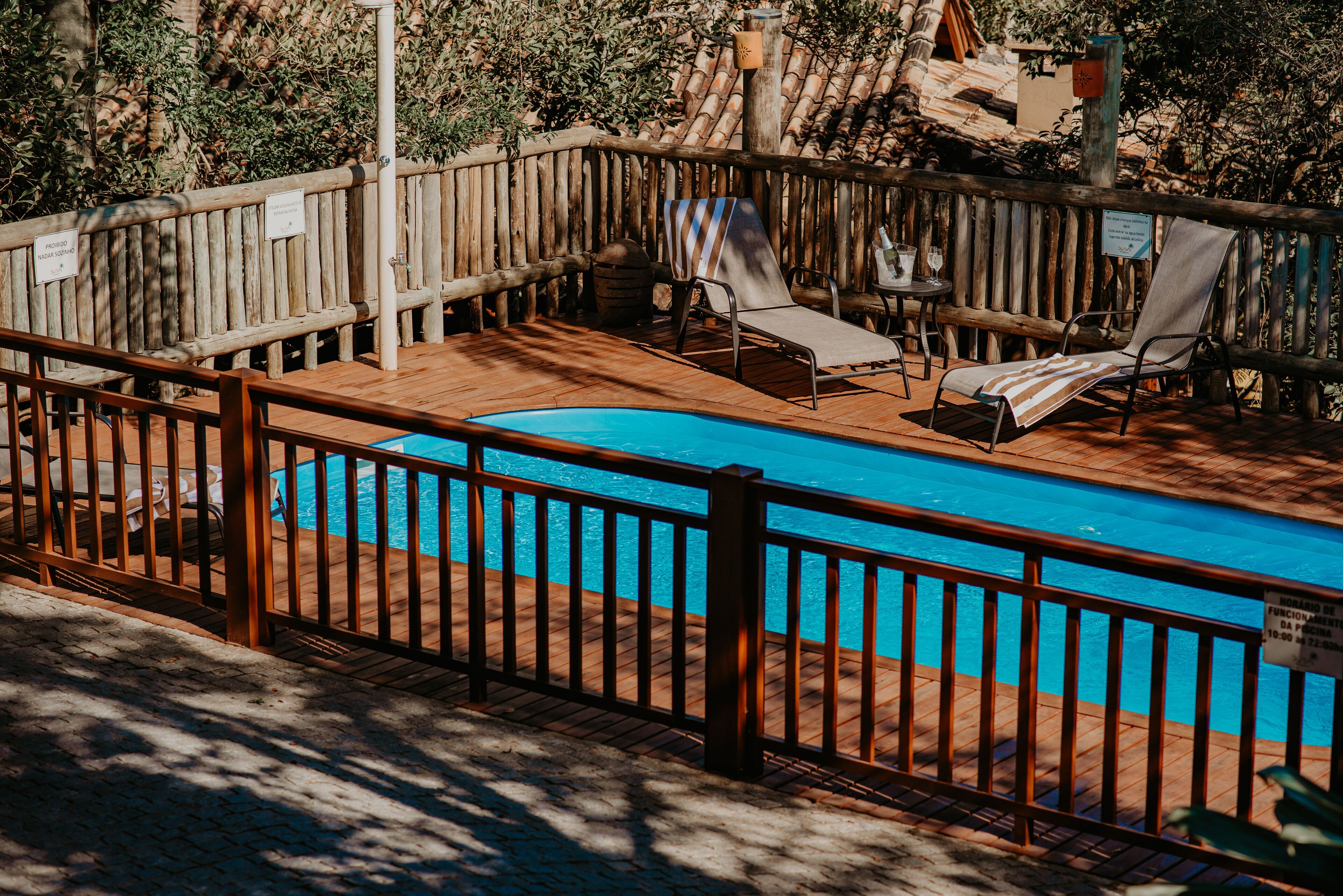 Zona de piscina con terraza de madera, sillones de descanso y piscina cercada.