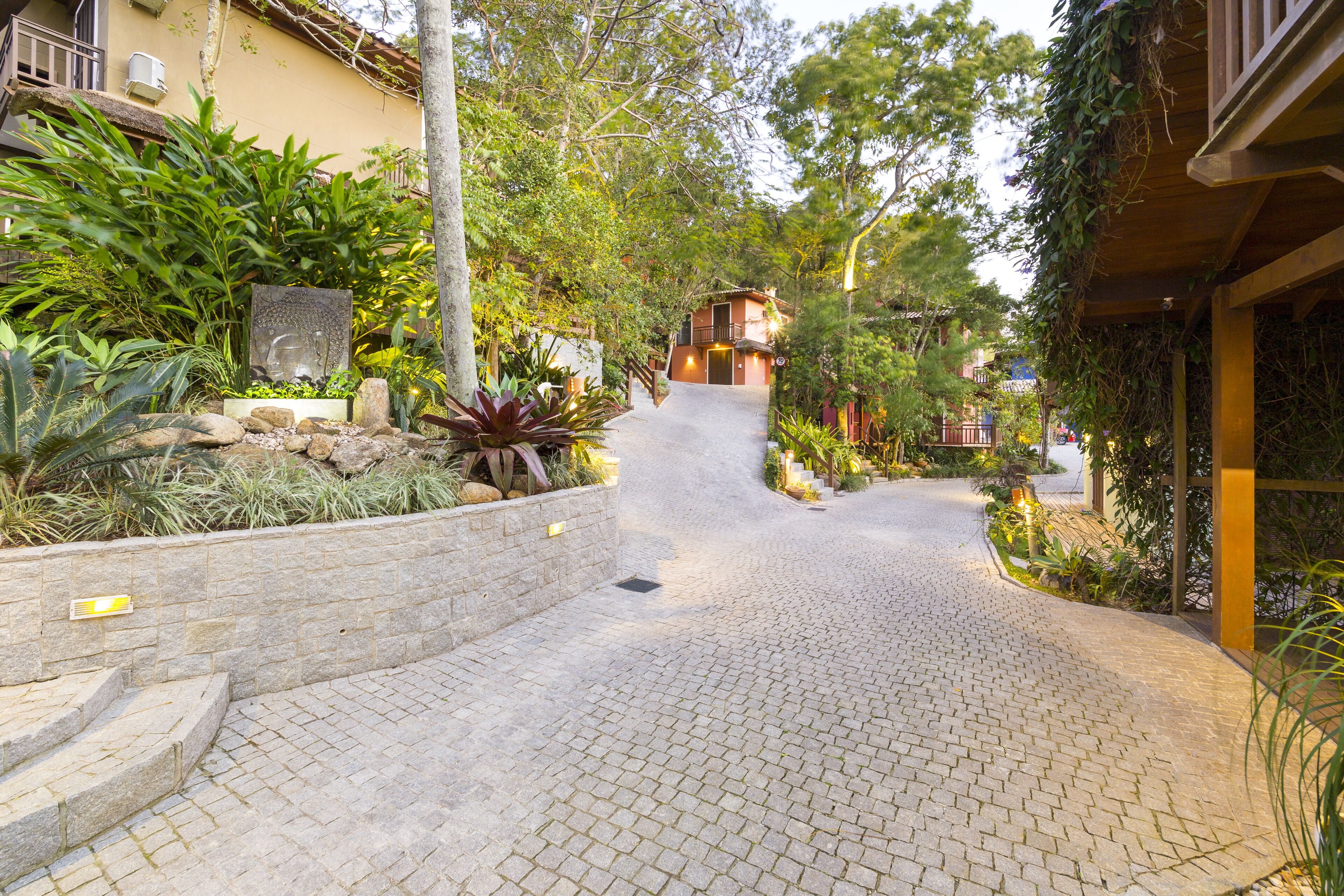 A cobblestone pathway leading to a building with a balcony and a stone wall with plants.