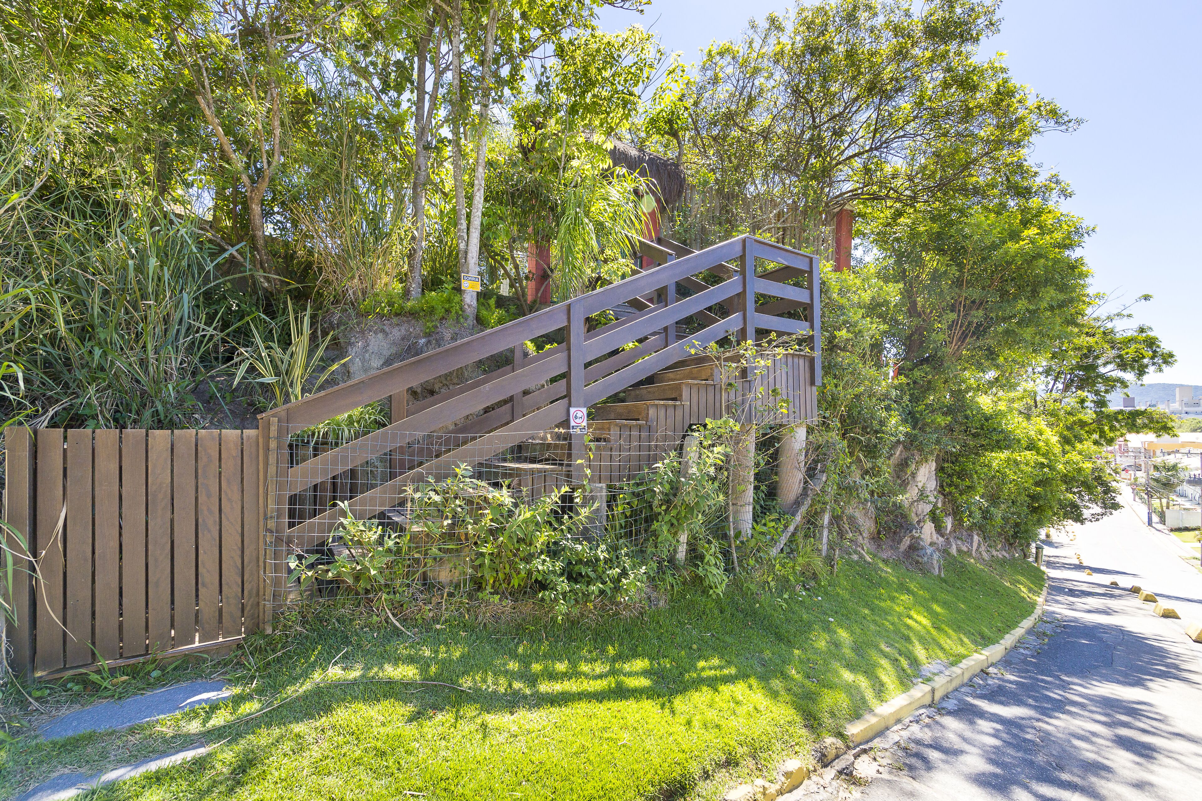 A wooden staircase with a metal railing leading up to a building, surrounded by greenery and trees.
