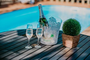 A poolside setting with a bottle of champagne in a bucket, two glasses, and a small potted plant.