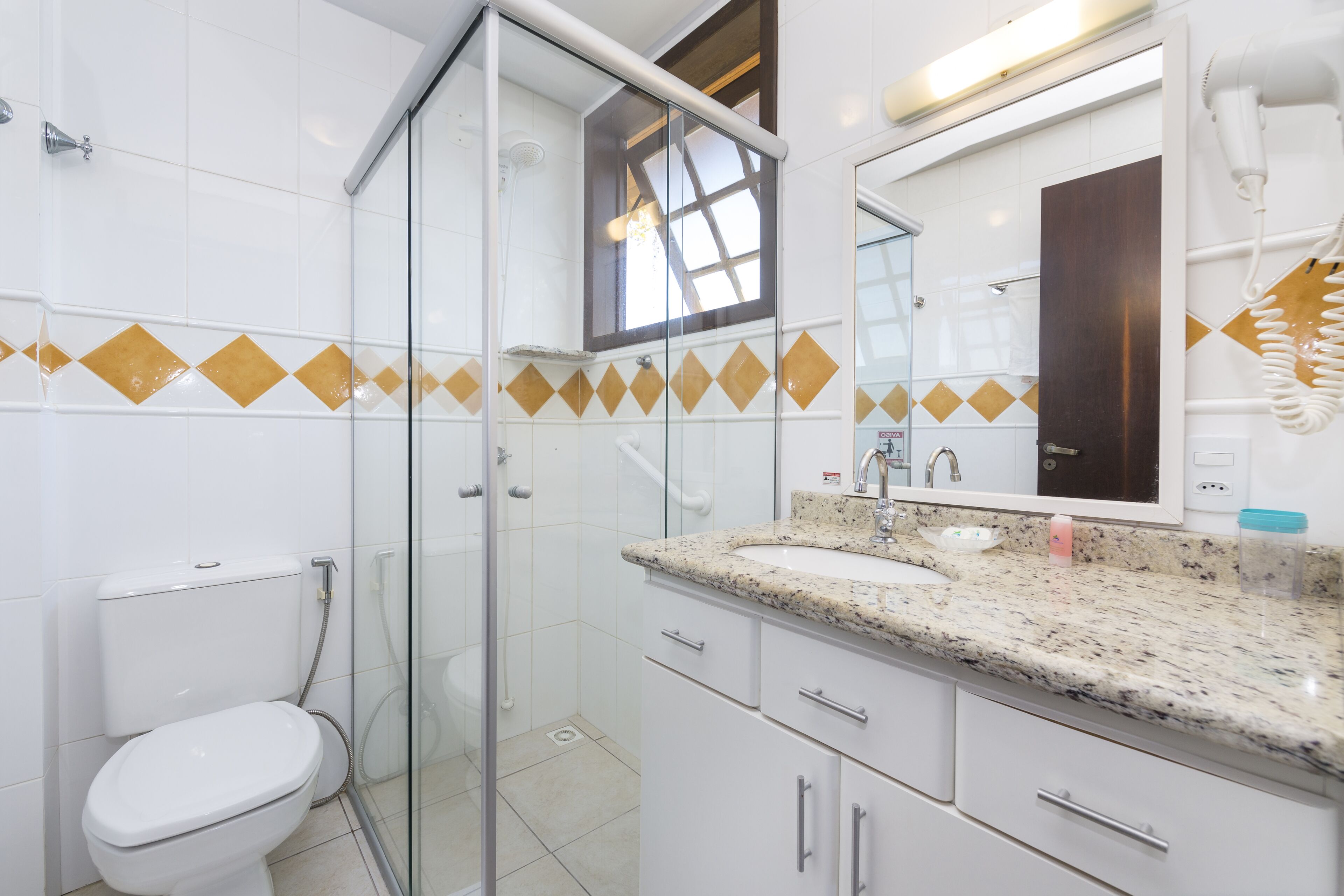 Ein modernes Badezimmer mit Duschkabine aus Glas, einer weißen Toilette, einem Waschbecken mit Granitplatte und einem großen Spiegel darüber.