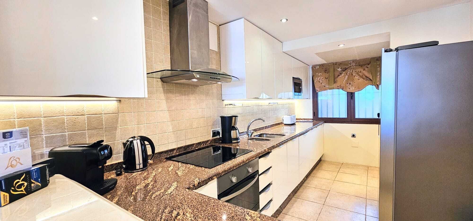 A modern kitchen with a granite countertop, stainless steel appliances, and a window with curtains.