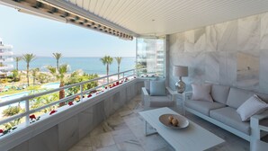 Un balcón con vista al mar, un sofá blanco, una mesita y una lámpara.