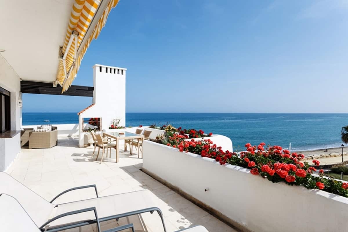 A terrace with outdoor seating, a white column, and a view of the sea.
