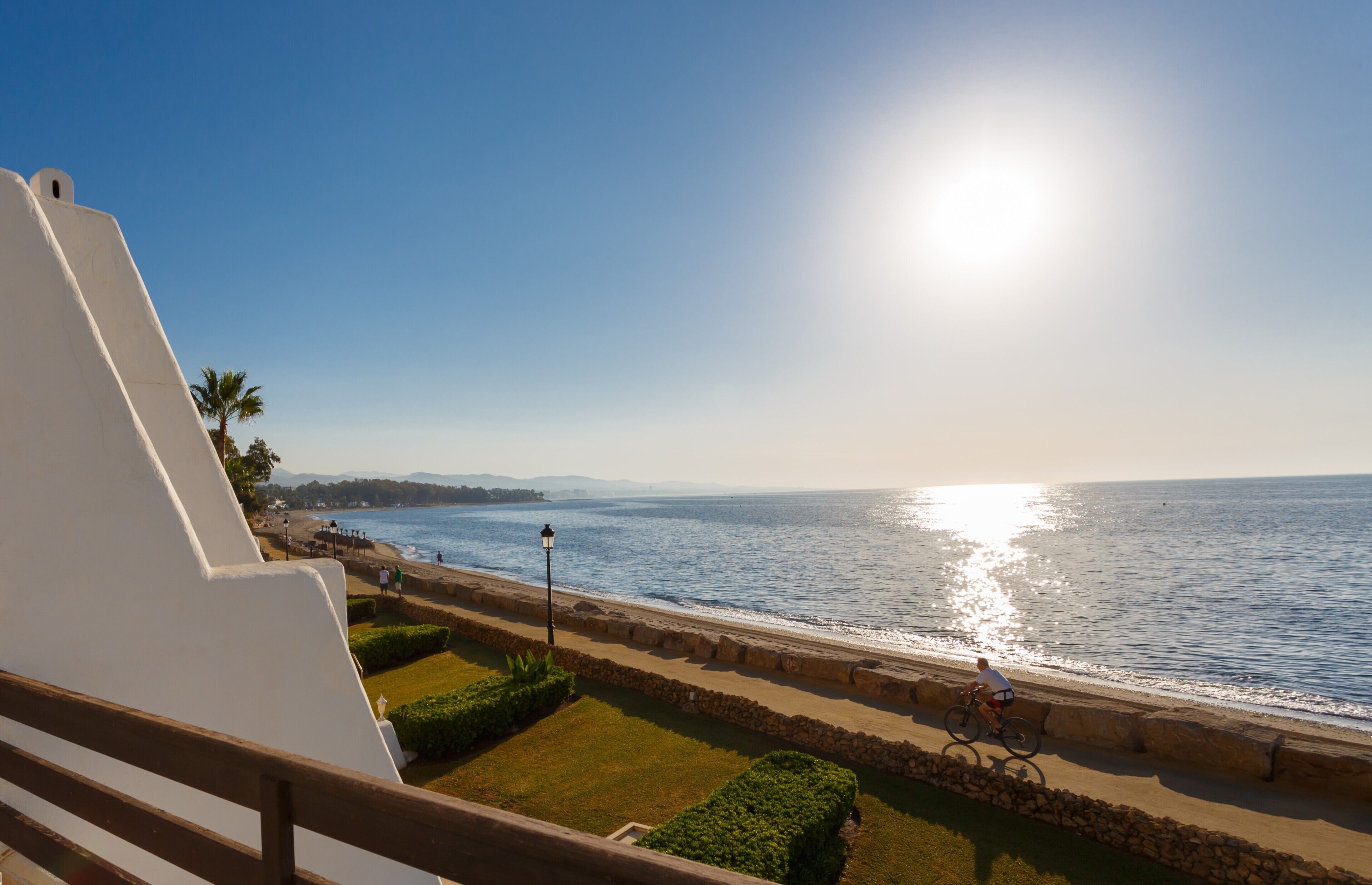 A coastal view with a clear sky, a paved walkway, and a cyclist.