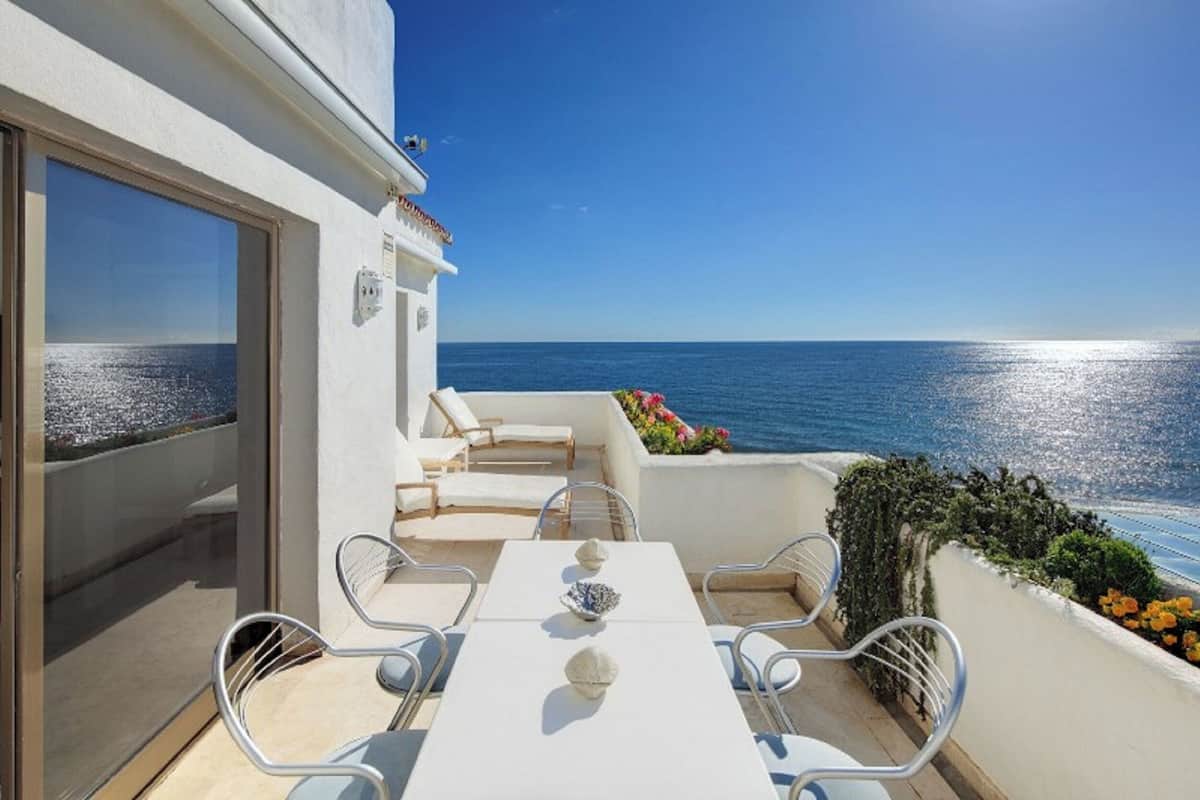 A balcony with a white table and chairs, overlooking the sea.