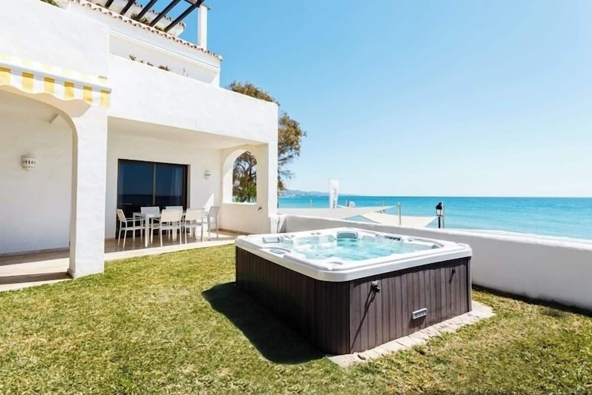 A modern outdoor area with a hot tub, a pool, and a patio with chairs and a table.