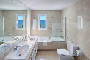 A modern bathroom with a large bathtub, a separate shower area, and a toilet. There are two sinks and a large mirror.