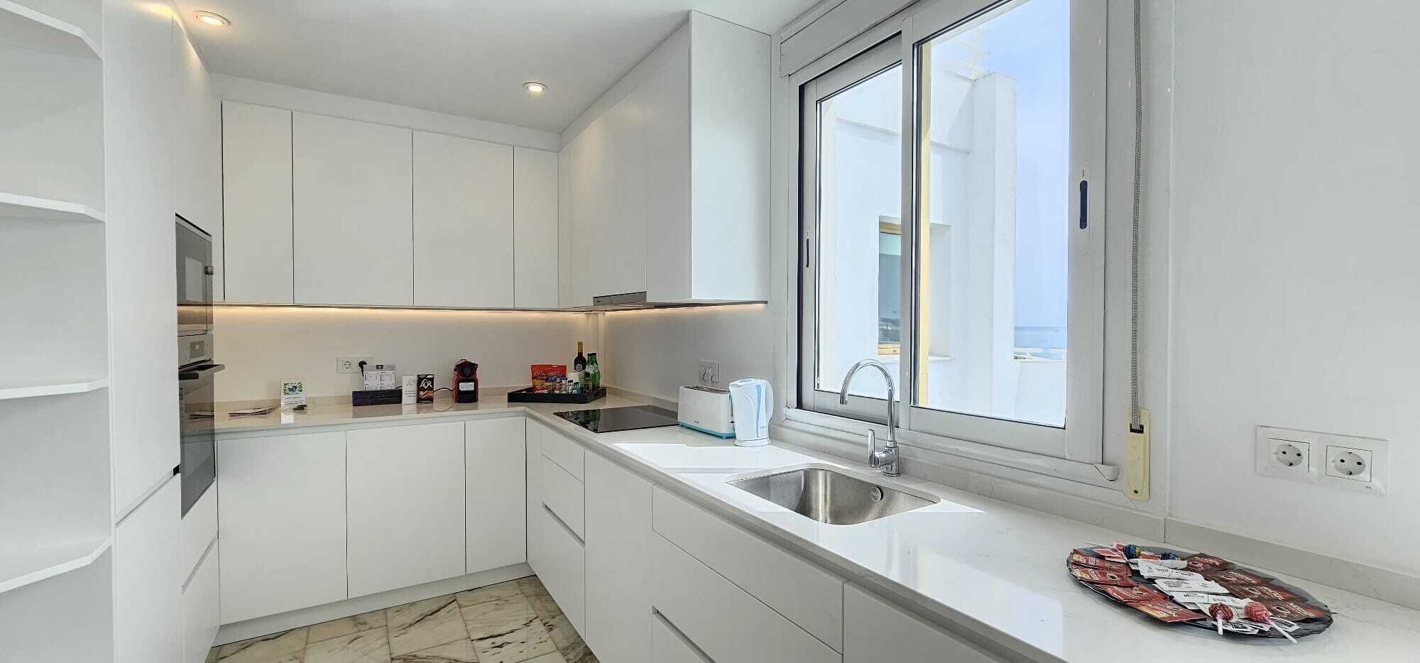 Eine moderne Küche mit weißen Schränken, einer Spüle aus Edelstahl und einem Fenster, das für natürliches Licht sorgt.