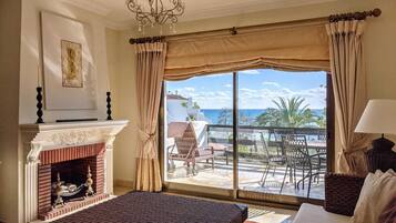 A hotel room with a large window, a fireplace, a bed, and a balcony with outdoor furniture.