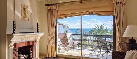 Une chambre d’hôtel dotée d’une grande fenêtre, d’une cheminée, d’un lit et d’un balcon aménagé avec du mobilier d’extérieur.